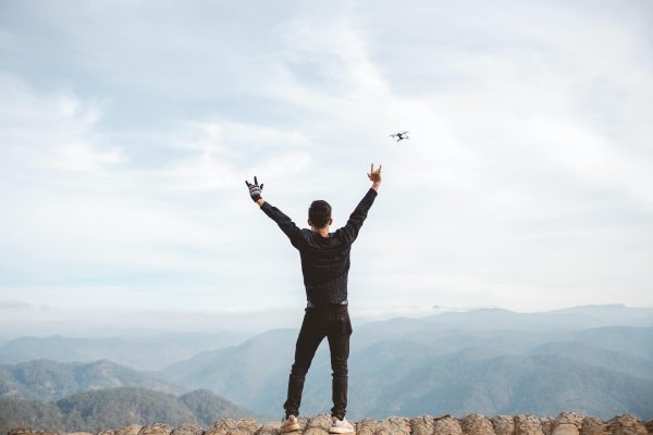 A man with arms raised on a mountain, capturing drone footage of breathtaking scenery. great lifestyle
